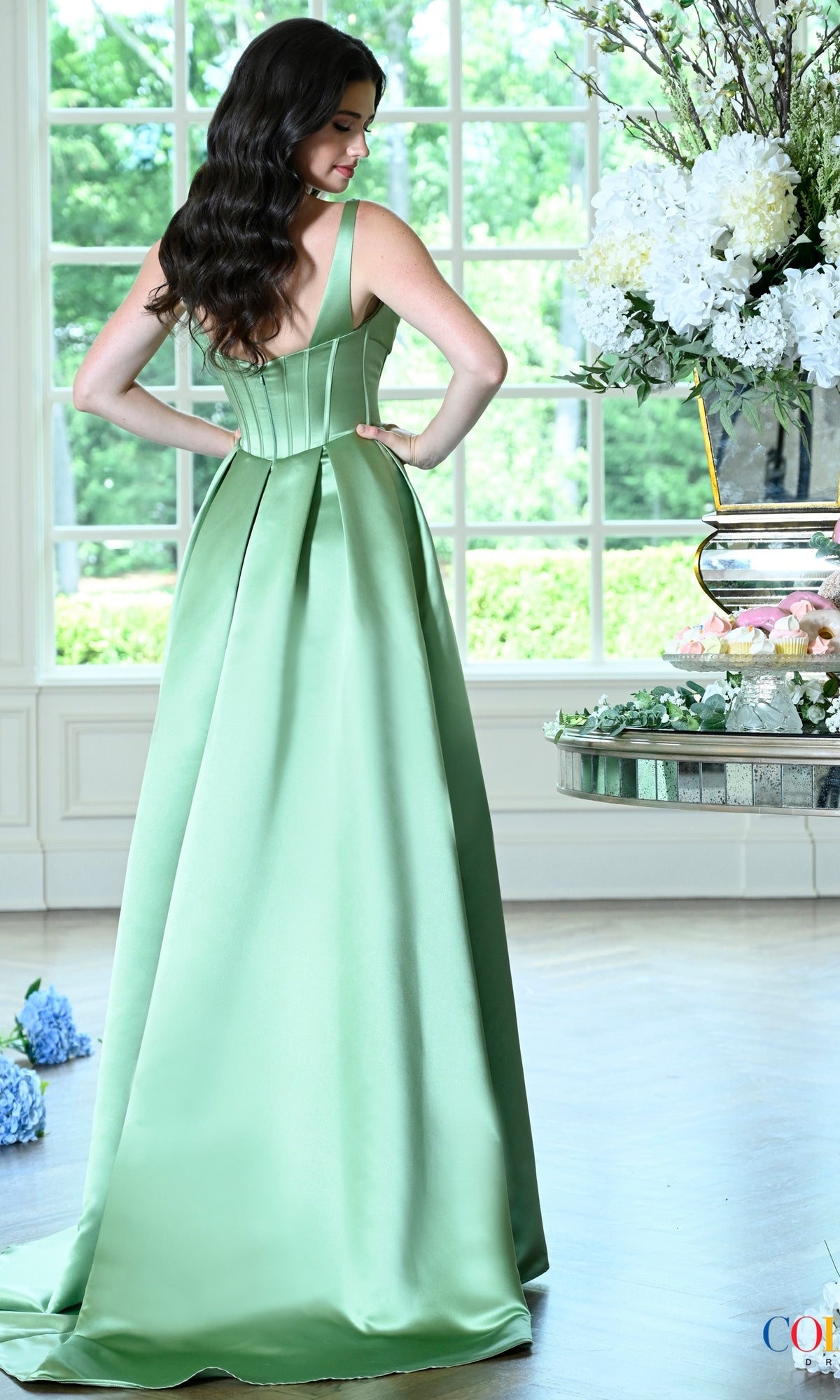 A woman wearing a sage green satin Long Prom Dress: Colors Dress 4001 with a corset-style bodice and a full skirt.
