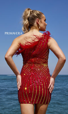 A woman stands on the beach facing the ocean, wearing the One-Shoulder Sequin Party Dress with Feathers 4002 in sparkly red and gold, her back to the camera.