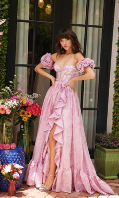 A woman stands before glass doors in the Ava Presley 40035 long formal dress, featuring a corset bodice pink gown with ruffled details and detached puff sleeves, surrounded by vibrant flowers and chic outdoor decor.