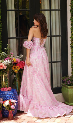 A woman wearing the Ava Presley 40035 long formal dress stands with her back to the camera, surrounded by potted flowers and plants near glass doors.