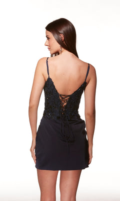 A woman faces away, wearing the Sheer-Corset Short Homecoming Dress Alyce 40036 in navy blue, featuring thin shoulder straps and a lace-up back.