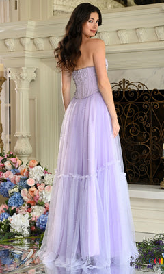 A woman wears a lavender strapless tulle Colors Dress 4003 prom dress with a beaded corset bodice and a tiered floor-length skirt.