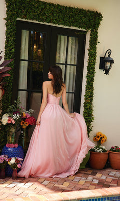 A woman wearing the Ava Presley 40041 A-Line Long Strapless Prom Dress stands outside glass doors, holding her gown amid colorful flower arrangements in pots and vases.