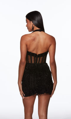 A woman faces away in a black Alyce 40043 short homecoming dress, featuring bead detailing and a halter neckline, set against a plain white background.