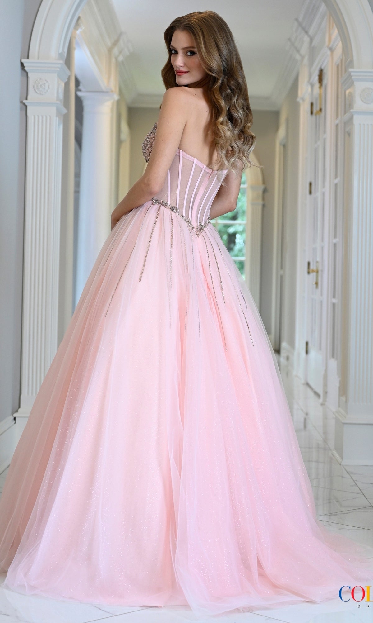 A woman wearing a pale pink, strapless glitter Long Prom Dress: Colors Dress 4004 with a beaded corset bodice.
