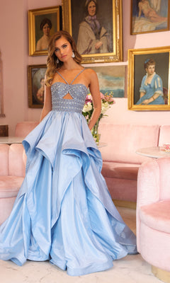 A woman wears the sparkly light blue Horsehair-Hem Prom Ball Gown: Ava Presley 40054 in a pink room with framed portraits and a pink sofa in the background.