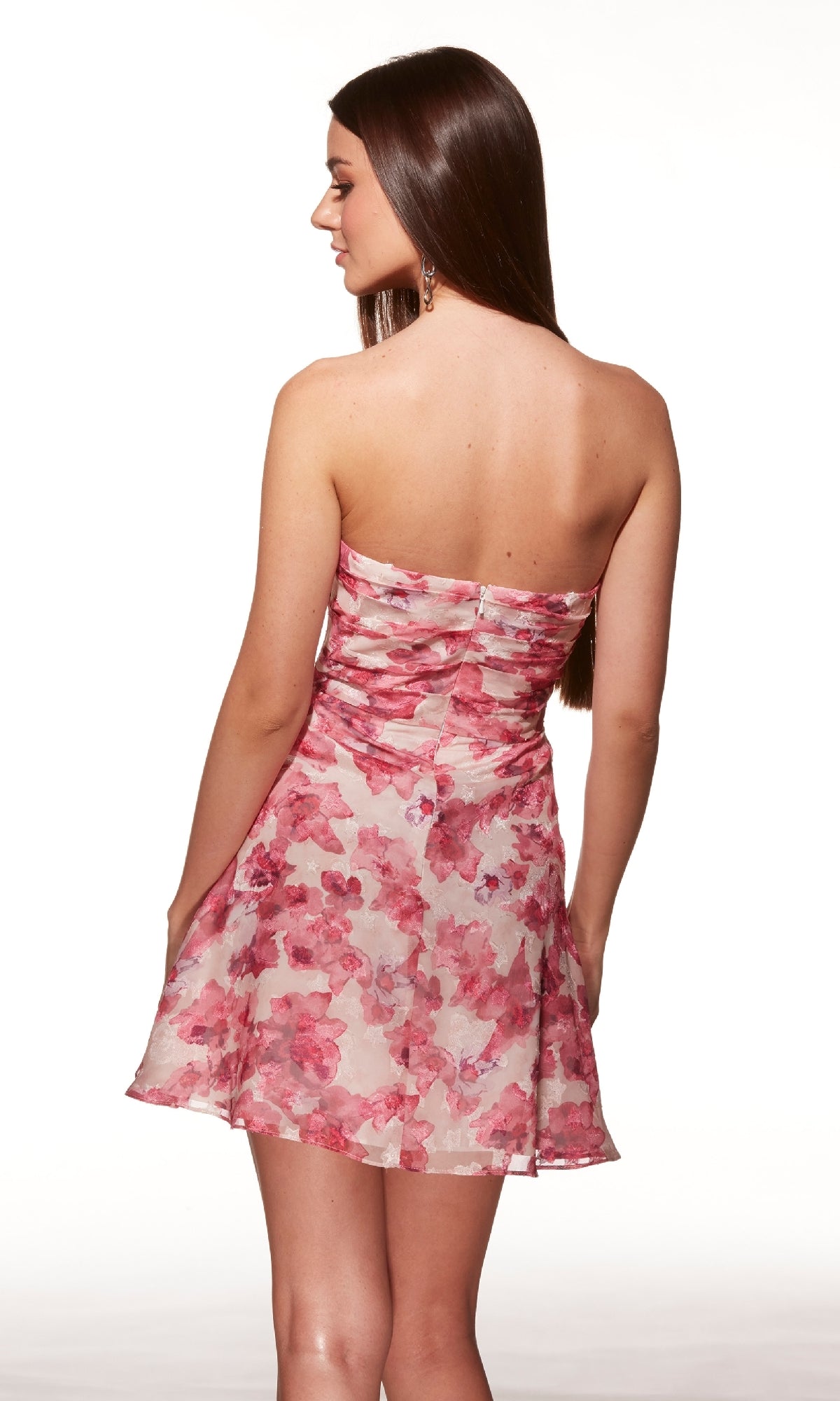 A woman with long brown hair is shown from the back wearing the Alyce 40079 short homecoming dress, which features a strapless design and a pink floral print, set against a white background.