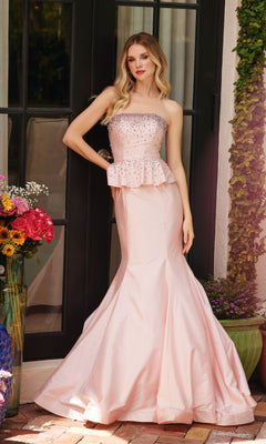 A woman stands before glass doors wearing the Ava Presley 40092 strapless peplum prom dress in light pink with beaded details. Nearby, flowers are arranged in vases.