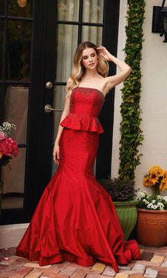 A woman in the Ava Presley 40092 strapless peplum prom dress stands outside by a black door, surrounded by potted flowers and greenery.