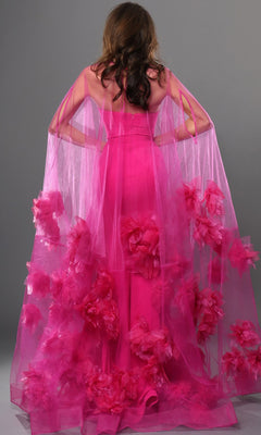 A person is seen from the back wearing the Long Formal Dress: Jovani 40092, a bright pink designer gown with a sheer overlay and large pink floral decorations, standing against a gray background.