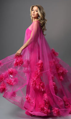 A woman wearing the Jovani 40092 long formal dress in bright pink, featuring sheer fabric and floral accents, stands against a gray background and looks over her shoulder.