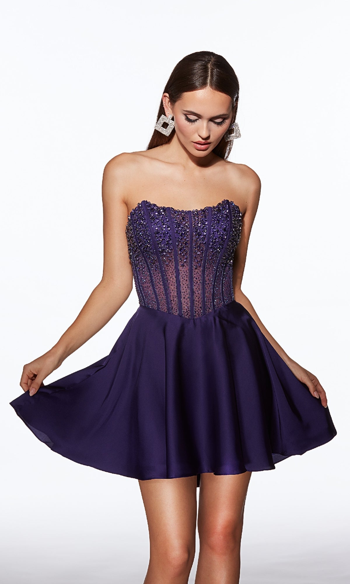 A woman stands against a plain white background wearing the Alyce 40101 Strapless Short Corset Hoco Dress, featuring a beaded corset and flared dark purple skirt.