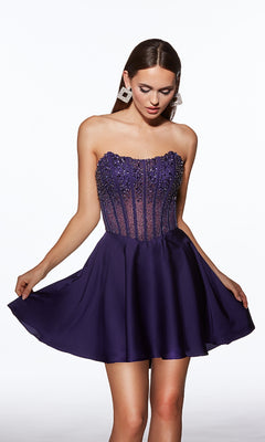 A woman stands against a plain white background wearing the Alyce 40101 Strapless Short Corset Hoco Dress, featuring a beaded corset and flared dark purple skirt.