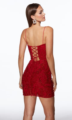 A woman faces backwards in front of a plain white background, showcasing the Alyce 40112 short homecoming dress—red with rhinestone embellishments and a lace-up open back.