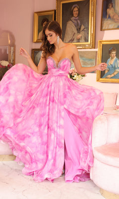 A woman wearing the Ava Presley 40116 Strapless Tie-Dye Prom Dress stands in a room with pink furniture and several portrait paintings on the walls.