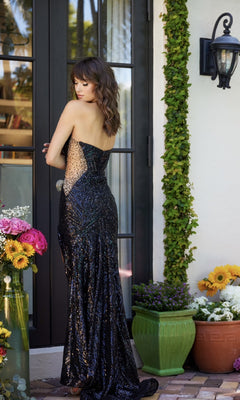 A woman in a strapless black Sparkly Sequin Prom Dress: Ava Presley 40121 stands outside a glass door, surrounded by potted flowers and lush greenery.