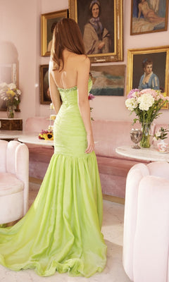 A woman in the Ava Presley 40129 Long Lime Green Prom Dress stands with her back to the camera in an elegant room featuring pink furniture and framed portraits on the wall.