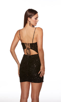 A woman stands facing away from the camera in a Short Black Sequin Bodycon Hoco Dress: Alyce 40131, featuring lace-up back detailing and a sparkling, backless silhouette against a white background.