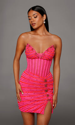 Woman in a fitted, hot coral/neon pink Alyce 40150 short homecoming dress with bead embellishments and a thigh-high slit, featuring a flattering strapless corset bodice, standing against a plain gray background.