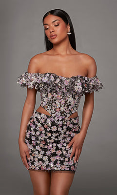 A woman poses against a plain gray background wearing the Alyce 40167 short homecoming dress in Black/Multi, featuring an off-the-shoulder neckline with ruffles, a fitted silhouette, floral print with 3D embroidered appliques on the cutout sides.