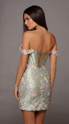 A woman stands against a plain gray background wearing the Alyce 40175 Short Homecoming Dress—a sage green, off-shoulder stretch-satin design featuring 3D floral embroidery and a lace-up back.