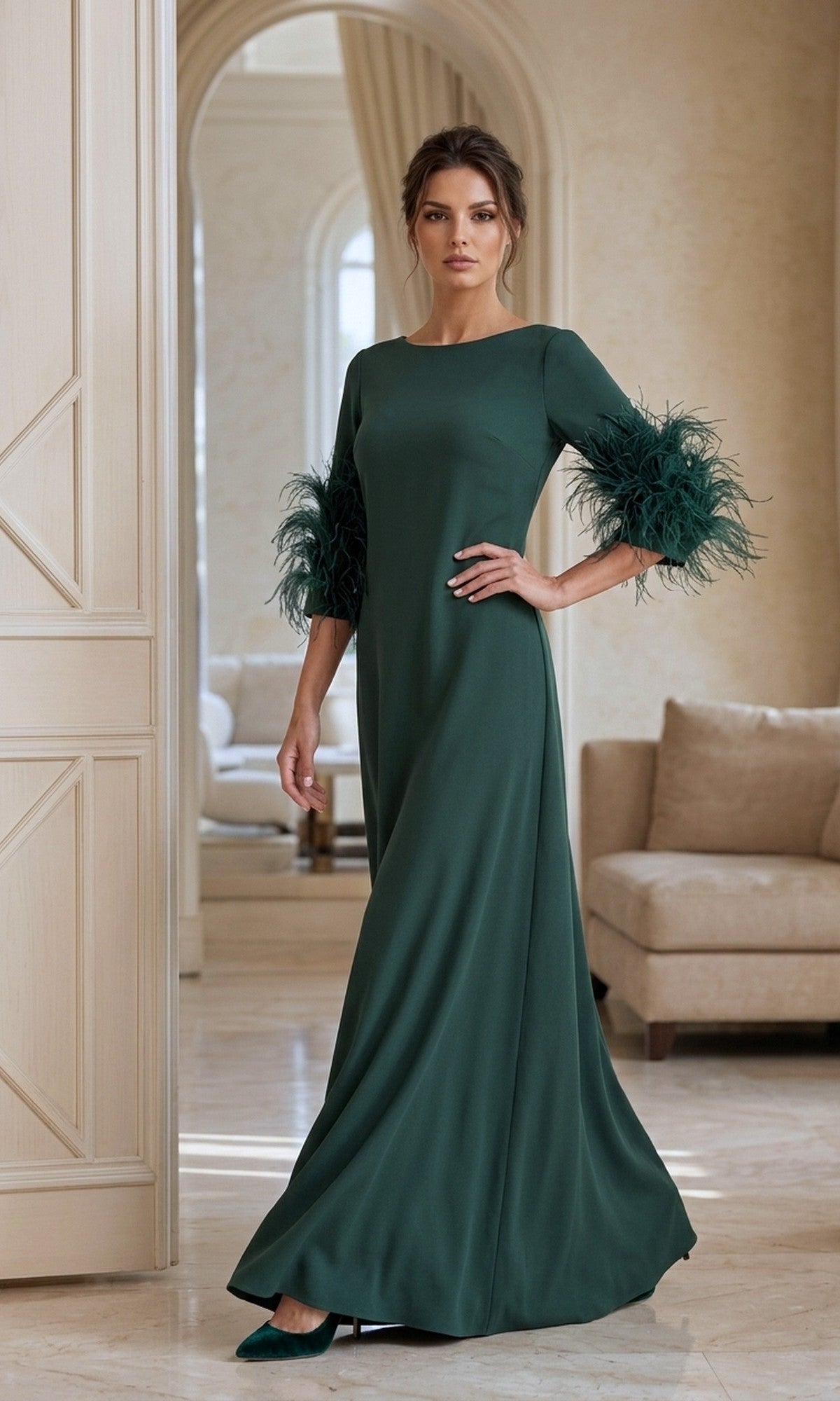 A woman stands indoors in a stylish, neutral-toned room, wearing the Long Formal Dress: Jovani 40200—a dark green gown with feathered sleeves.