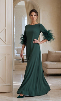 A woman stands indoors in a stylish, neutral-toned room, wearing the Long Formal Dress: Jovani 40200—a dark green gown with feathered sleeves.