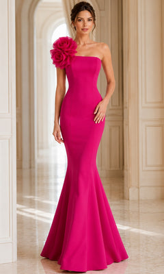 A woman stands in a bright, elegant hallway wearing the Long Formal Dress: Jovani 40201—a fitted, strapless, hot pink evening gown featuring a dramatic floral detail on one shoulder, reminiscent of classic Jovani designer style.