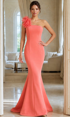 A woman stands in a bright room wearing the Long Formal Dress: Jovani 40201 in light coral, featuring a one-shoulder design with an elegant flower detail on the strap and a floor-length mermaid silhouette, exuding classic Jovani style.