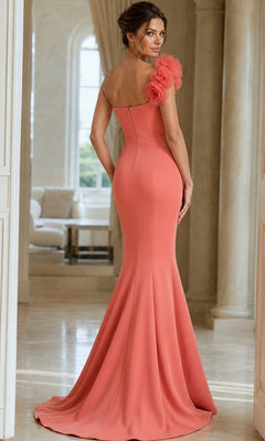 A woman wearing the Long Formal Dress: Jovani 40201, a fitted coral designer gown featuring floral detail on one shoulder, stands in a bright, elegant room with arched windows and columns.