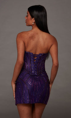 Wearing the Alyce 40205 short homecoming dress in vibrant purple, a woman with long dark hair stands against a plain gray background. The strapless dress features shimmering bead details and a lace-up back for added elegance.