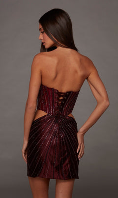 Wearing the Alyce 40211 short homecoming dress, a woman showcases a strapless maroon design with a corset bodice adorned with bead embellishments and lace-up back detailing. The fitted silhouette stands out elegantly against a plain gray background.