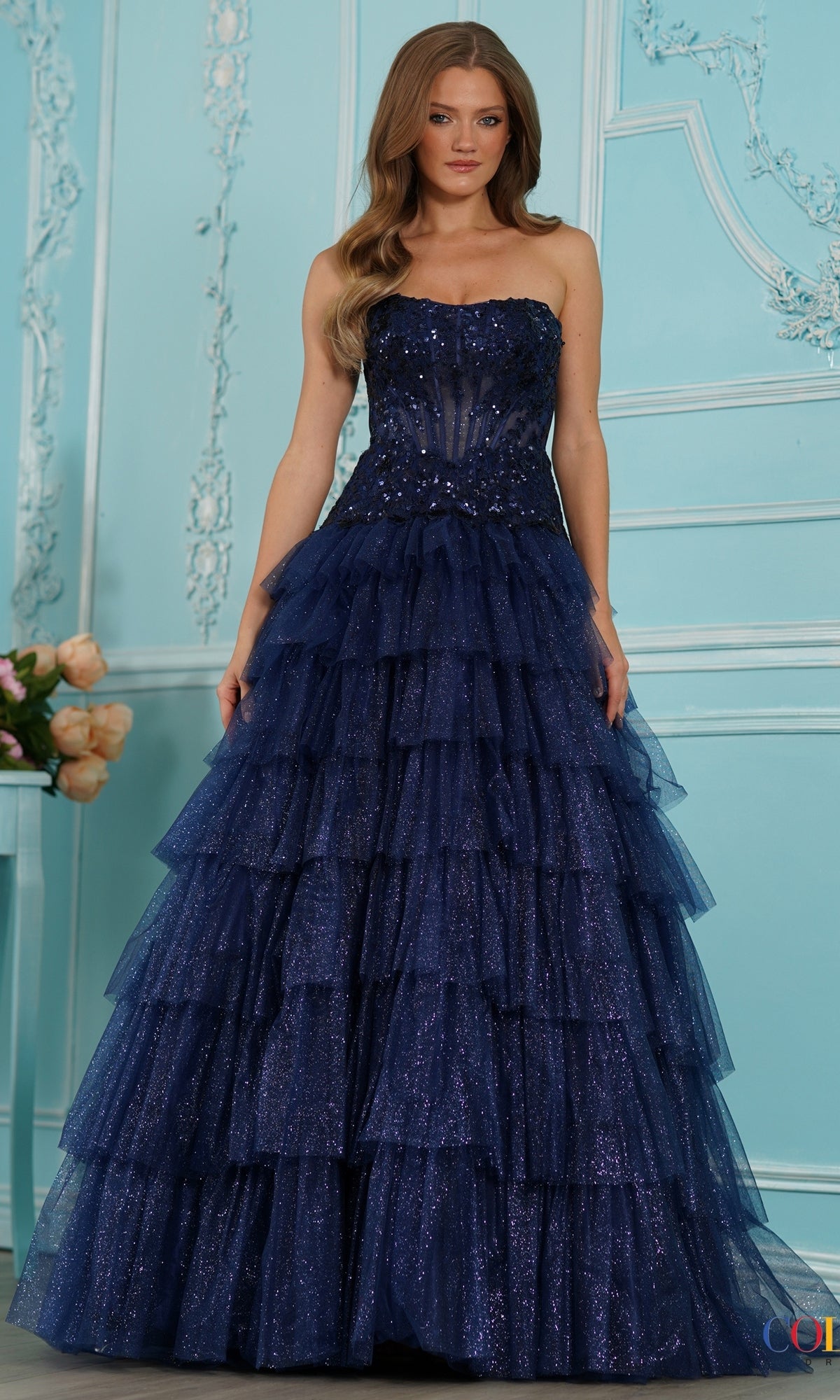 A woman wears a navy Long Prom Dress: Colors Dress 4024, featuring a strapless sequin bodice and a tiered tulle skirt.