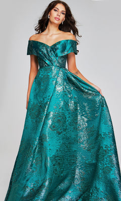 Wearing the Long Formal Dress: Jovani 40296, a woman stands against a plain background, elegantly holding part of the off-the-shoulder metallic textured gown with a floral pattern to the side.