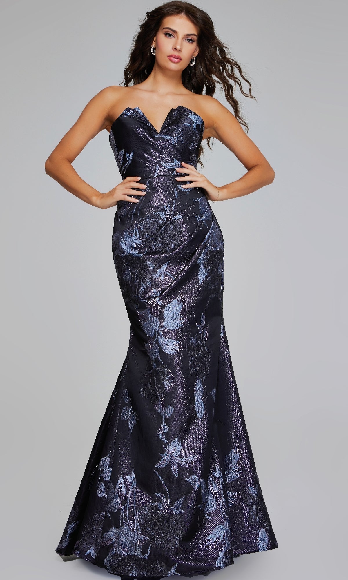 Model showcases the Jovani 40309 long formal dress—a strapless, dark blue floor-length mermaid gown with a subtle floral print—posing with hands on hips against a plain light gray background.