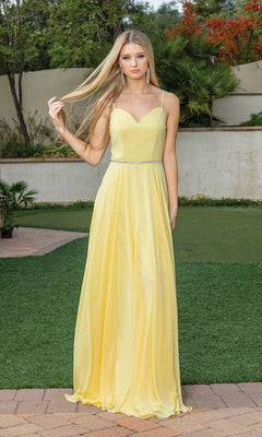 A woman stands on a stone path in a garden wearing the Simple Long A-Line Prom Dress with Corset Back—a sleeveless yellow gown featuring thin straps, a beaded waistline, and corset back—while holding a strand of her hair.