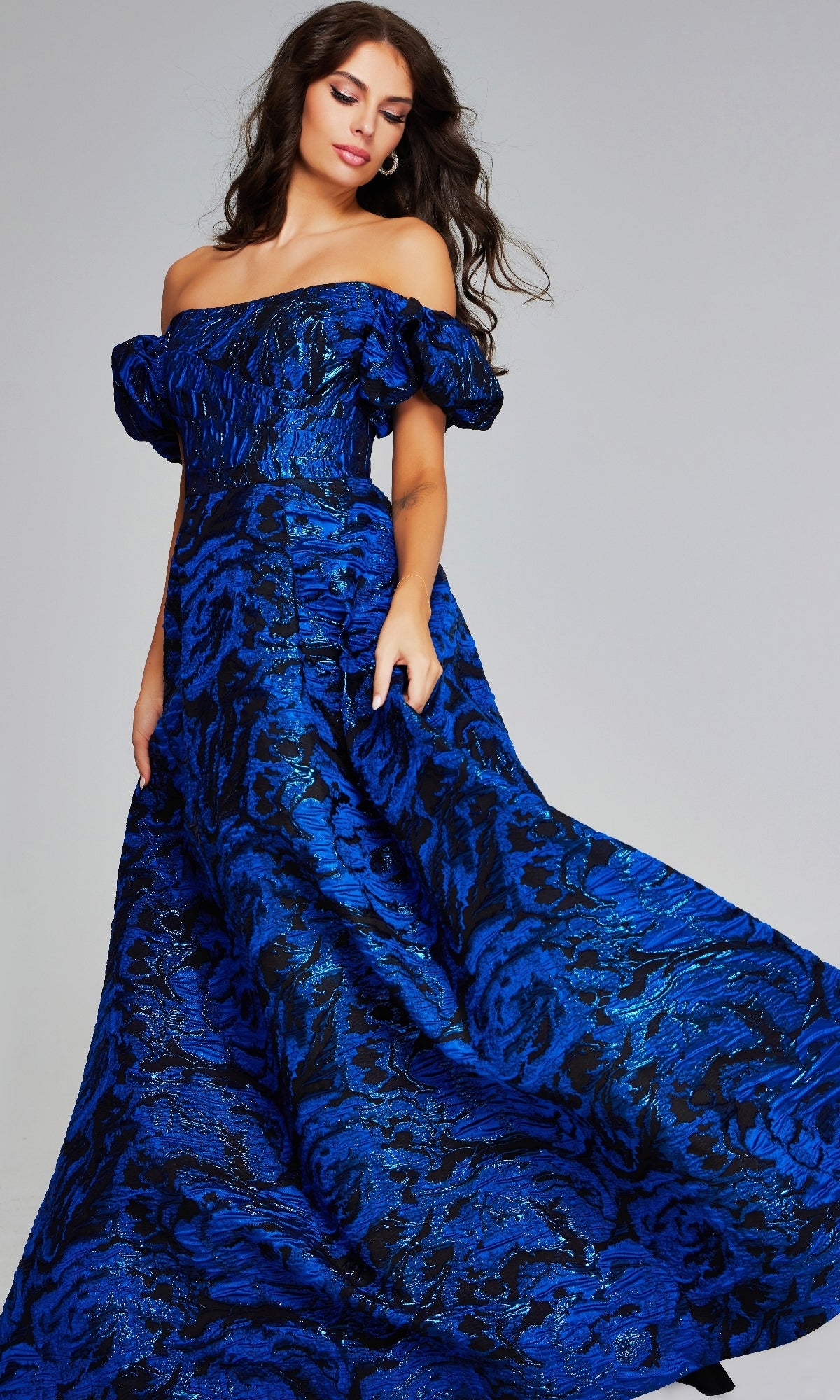A woman wears the Jovani 40315 long formal dress—an off-the-shoulder ball gown with puff sleeves and blue-black patterned fabric, perfect for special occasions.