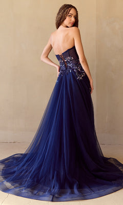 A woman wearing the Strapless A-Line Prom Gown: Amelia Couture 4031, featuring a sequin corset bodice, sheer tulle skirt, and floral embroidery in navy blue, faces away and looks over her shoulder.