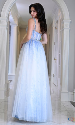 A woman in a hallway wearing a Long Prom Dress: Colors Dress 4033, a floor-length, baby blue gown with a white ombré floral print, a crystal-beaded bodice, and spaghetti straps.