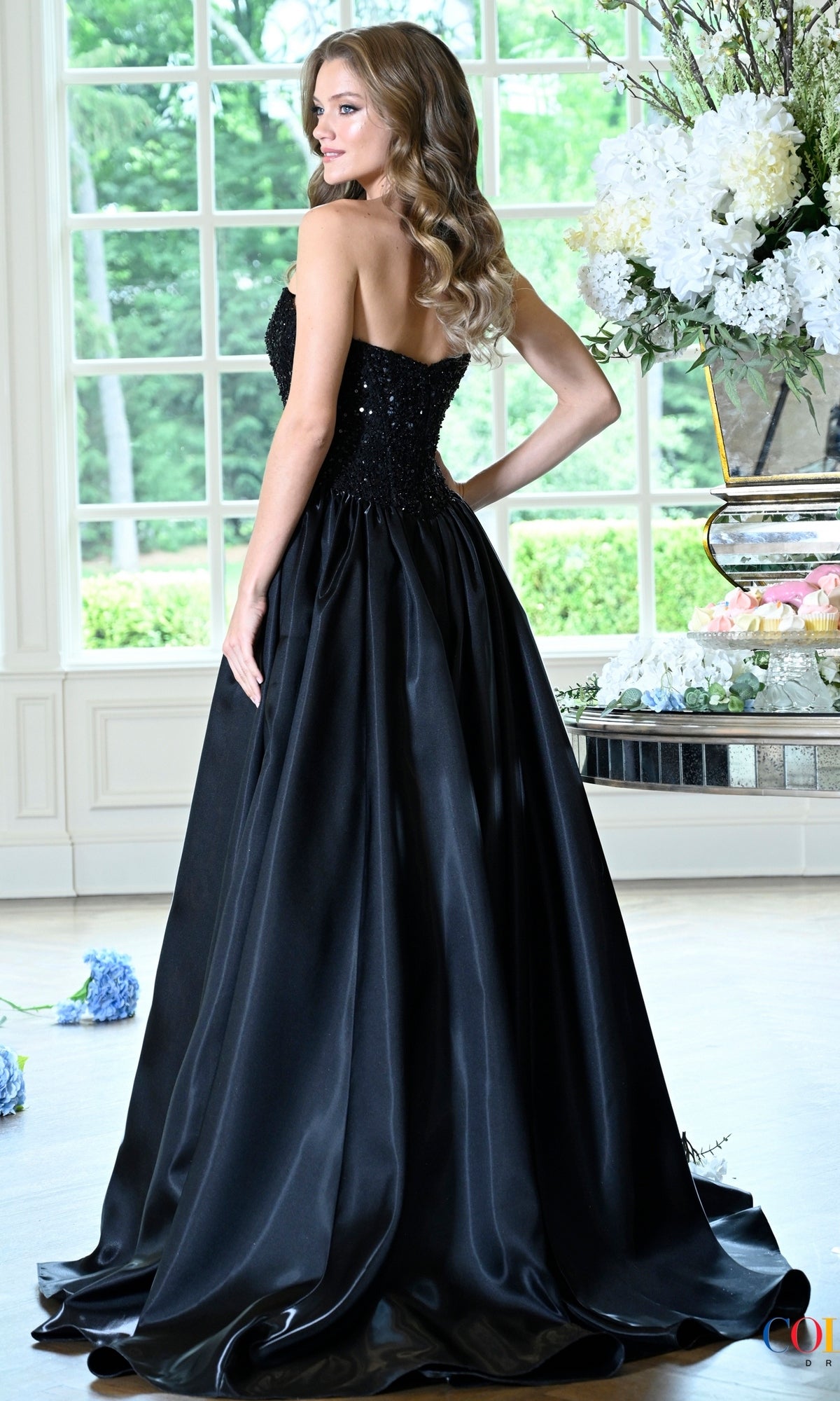 Woman wearing a strapless black Long Prom Dress: Colors Dress 4034 with a sequined bodice and a full floor-length skirt.