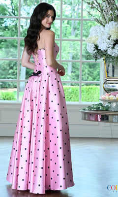 A person wears a pink and black polka dot Retro Polka Dot Prom Dress: Colors Dress 4035, featuring a strapless, floor-length silhouette and a lace-up back closure.