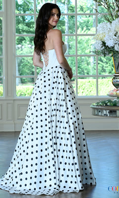 A woman wears a Colors Dress 4036 long prom dress, a white floor-length gown featuring a black polka-dot skirt and a strapless sweetheart corset bodice.