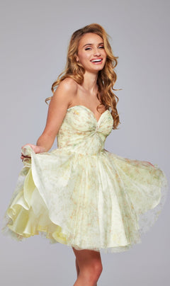 A woman in the Strapless Short Yellow Hoco Dress Jovani 40374, featuring a floral pattern, poses smiling against a plain background while holding out the skirt.