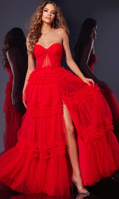 A woman wearing the Jovani 40466 Strapless Prom Ball Gown with a corset bodice, layered tulle skirt, and thigh-high slit stands by a mirror in transparent heels.