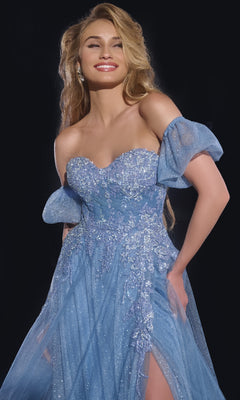 A woman smiles with one hand on her hip, posing against a dark background in the shimmering Long Blue Prom Dress: Jovani 40474, featuring off-the-shoulder sleeves and floral embellishments.