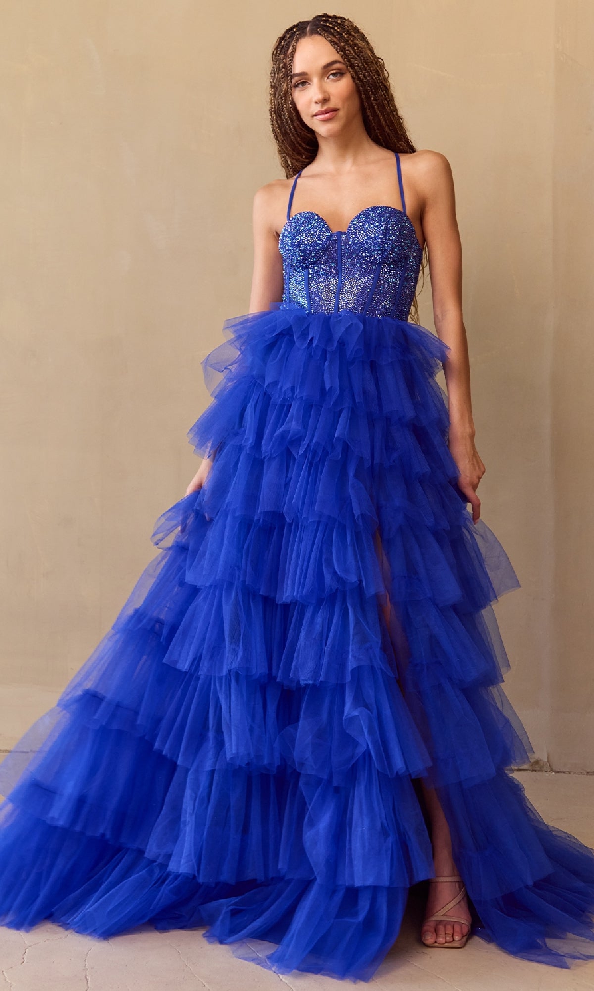 Woman wearing a royal blue tiered ball gown with a beige background