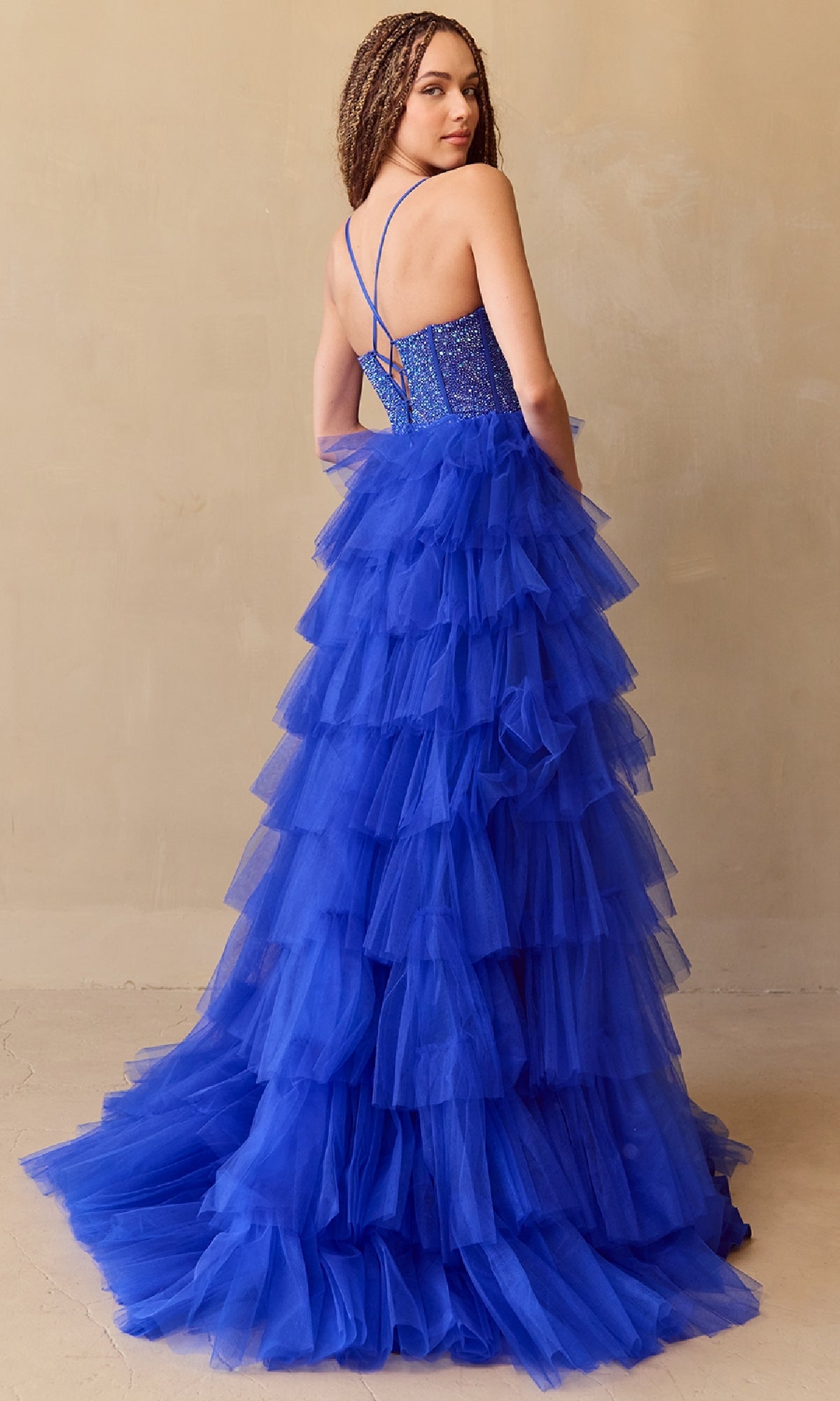 Woman modeling the back of a royal blue tiered ball gown with an intricate top on a beige background