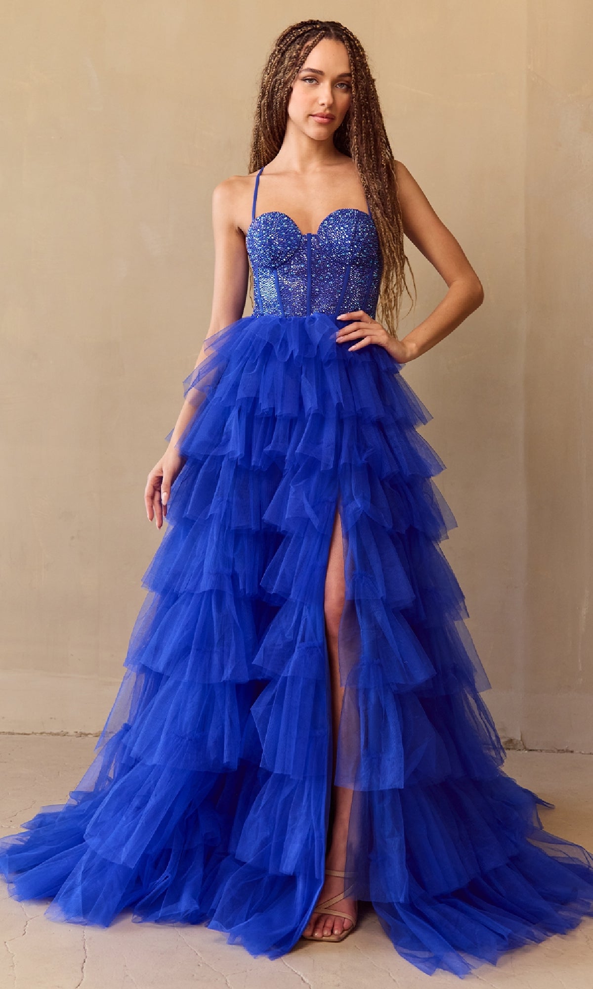 Woman wearing a royal blue tiered ball gown dress with a slit on a beige background