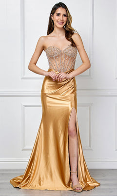 A woman stands indoors wearing the Amelia Couture 4049 Strapless Long Prom Gown, featuring a sheer embellished bodice and thigh-high slit, smiling at the camera.