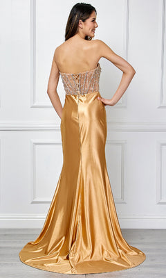 A woman stands with her back to the camera in the Amelia Couture 4049, a strapless long prom gown featuring a gold satin finish, beaded bodice, and flowing train.